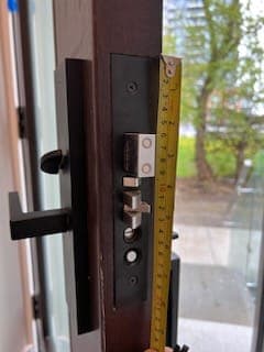 Yellow tape measure held against a black door lock plate to determine its height.