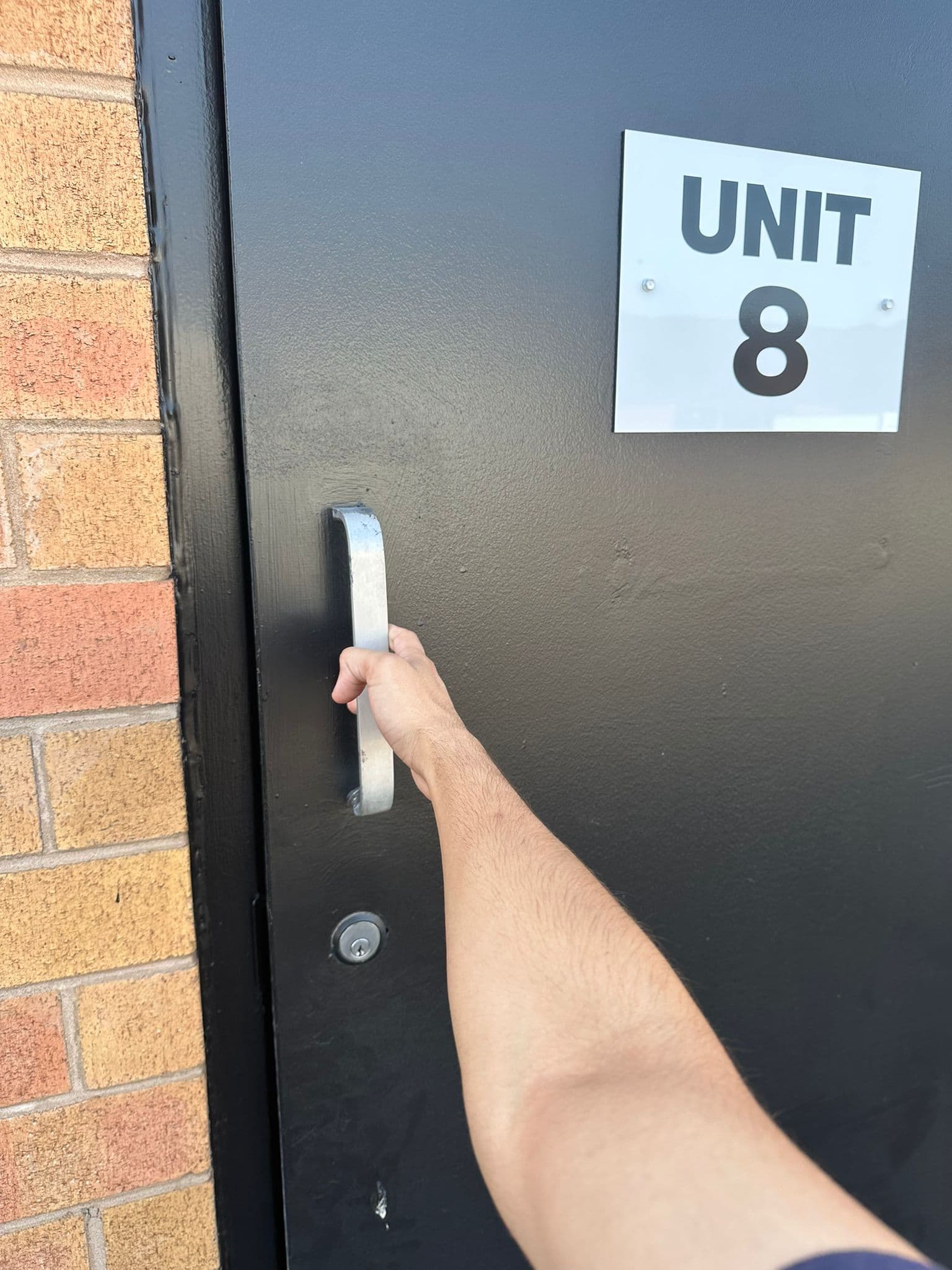 A person's hand grips the silver handle of a black door labeled Unit 8.